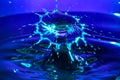 Brilliant burst of vibrant blue light against a dark violet waterdrop