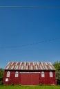 Broad side of a white and red barn with trees, blue sky, and power lines in the background Royalty Free Stock Photo