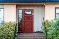 Image of brown wooden vintage entrance door with metal stairs and green bushes in front of it Royalty Free Stock Photo