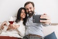 Image of brunette couple taking selfie photo together on sofa while drinking wine Royalty Free Stock Photo
