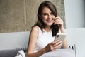 Image of brunette joyful woman using smartphone while resting on couch
