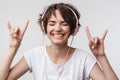 Image of brunette woman in basic t-shirt showing rock sign while listening to music with headphones Royalty Free Stock Photo