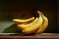 Image of bunch of ripe yellow bananas on wooden background, bright sunlight, harvest in wooden box