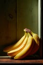 Image of bunch of ripe yellow bananas on wooden background, bright sunlight, harvest in wooden box