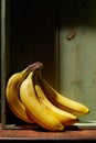 Image of bunch of ripe yellow bananas on wooden background, bright sunlight, harvest in wooden box