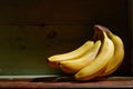 Image of bunch of ripe yellow bananas on wooden background, bright sunlight, harvest in wooden box