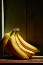 Image of bunch of ripe yellow bananas on wooden background, bright sunlight, harvest in wooden box