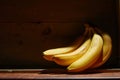 Image of bunch of ripe yellow bananas on wooden background, bright sunlight, harvest in wooden box