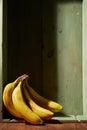 Image of bunch of ripe yellow bananas on wooden background, bright sunlight, harvest in wooden box