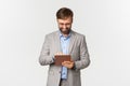 Image of businessman working, looking at digital tablet and smiling pleased, standing in grey suit and glasses over Royalty Free Stock Photo