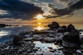 An image of a calm lake with a rocky shore at sunset.