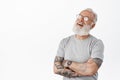 Image of candid senior man in glasses, laughing with arms crossed on chest, looking left aside with joyful relaxed face