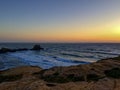 The image captures a beautiful sunset over a rugged coastline with waves crashing against the rocks Royalty Free Stock Photo