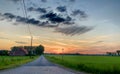 Dramatic Sunrise Over Rural Road with Farmhouse and Lush Fields Royalty Free Stock Photo