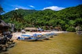 several boats parked along side of a mountain shore with small huts on the other side