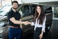 Portrait of car dealer handshaking with happy female in automobile center