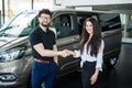 Portrait of car dealer handshaking with happy female in automobile center