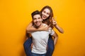 Image of caucasian couple having fun while man piggybacking joyful woman, isolated over yellow background Royalty Free Stock Photo