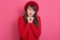 Image of caucasian darkhaired modest woman wearing red beret and sweater, model posing isolated over rosy background in studio, Royalty Free Stock Photo