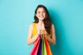 Image of cheerful girl going shopping, holding bags with purchases and smiling at camera, standing against blue Royalty Free Stock Photo