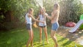 Image of cheerful laughing girls in wet clothes dancing in the garden and holding water hose. Family playing and having Royalty Free Stock Photo