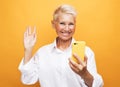 Image of cheerful mature old woman standing isolated over yellow background wall talking by mobile phone Royalty Free Stock Photo