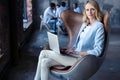 Image of cheerful office woman with blond hair in business wear sitting on chair and working with laptop office.