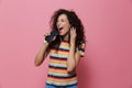 Image of cheerful woman 20s with curly hair singing while holding smartphone like microphone and listening to music via earphones Royalty Free Stock Photo