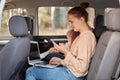 Image of cheerful young woman working on laptop while sitting with her baby daughter in safety chair on backseat of car. female Royalty Free Stock Photo