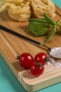 Image of cherry tomatoes in the foreground on a bamboo table with flour, basil and pasta in the background Royalty Free Stock Photo