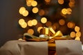Image of Christmas gift box with gold bow on background of defocused golden lights on New Year tree. Congratulating friends and Royalty Free Stock Photo