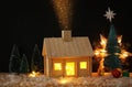 Image of christmas tree and wooden house with light through the window, over snowy table. Royalty Free Stock Photo