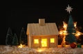 Image of christmas tree and wooden house with light through the window, over snowy table. Royalty Free Stock Photo