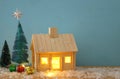 Image of christmas tree and wooden house with light through the window, over snowy table. Royalty Free Stock Photo