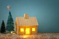 Image of christmas tree and wooden house with light through the window, over snowy table. Royalty Free Stock Photo