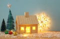 Image of christmas tree and wooden house with light through the window, over snowy table. Royalty Free Stock Photo