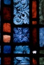 Image of close up detail of stained, leaded glass showing squares, rectangles of blues, reds, greens and painted pattern
