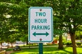 Close up of green Two Hour Parking sign in front of a park in summertime