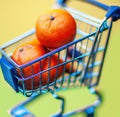 Image of close up of heap of oranges in blue min shopping trolley on yellow background