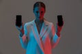 Image closeup of stylish woman 20s holding two mobile phones and showing black screens while standing under neon lights