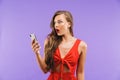 Image closeup of surprised or shocked woman 20s wearing red dress wondering or expressing surprise while holding mobile phone, st