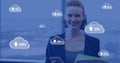 Image of cloud symbols uploading data over happy caucasian businesswoman with smartphone