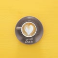 Image of coffe cup with foam of heart shape over wooden yellow background and text: WITH LOVE. Royalty Free Stock Photo