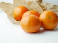 Image of a collection of four ripe oranges on a kitchen countertop, next to a brown paper bag