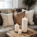 Composition of candles on white table against the background of sofa with plaids and pillows Cozy home concept