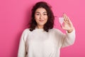 Image of confident charming brunette standing isolated over pink background in studio, holding mentrual cup in one hand, looking Royalty Free Stock Photo