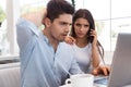 Displeased young loving couple sitting in cafe using laptop computer talking by phone Royalty Free Stock Photo