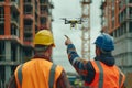 Construction site with two workers using a drone. One worker points at the drone. Building structures and tower cranes Royalty Free Stock Photo