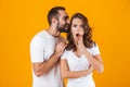 Image of content man whispering secret or interesting gossip to woman in her ear, isolated over yellow background