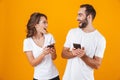 Image of couple man and woman smiling while both using mobile phones, isolated over yellow background Royalty Free Stock Photo